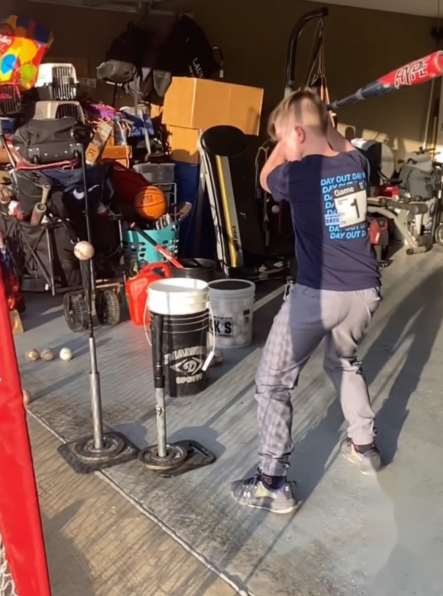 A young athlete working off a batting tee in the garage