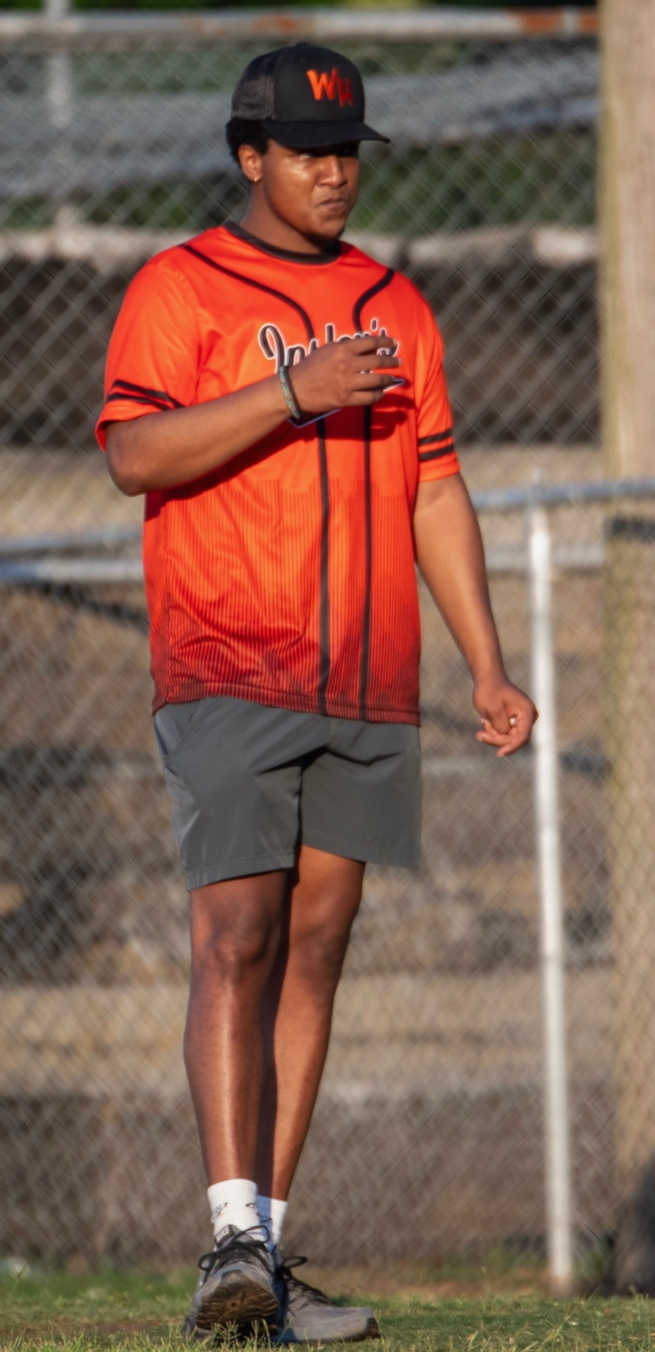A coach in a red jersey and black WH cap standing on the field