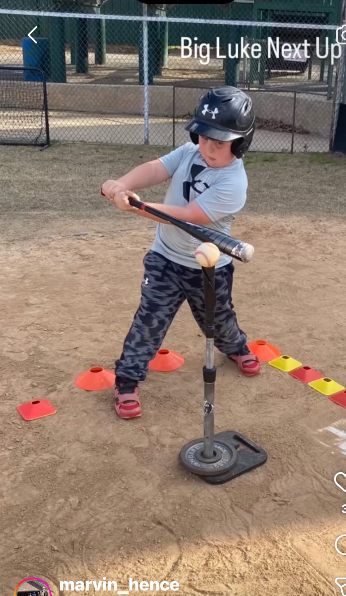 A young athlete in a helmet swinging at a ball on a batting tee surrounded by cones