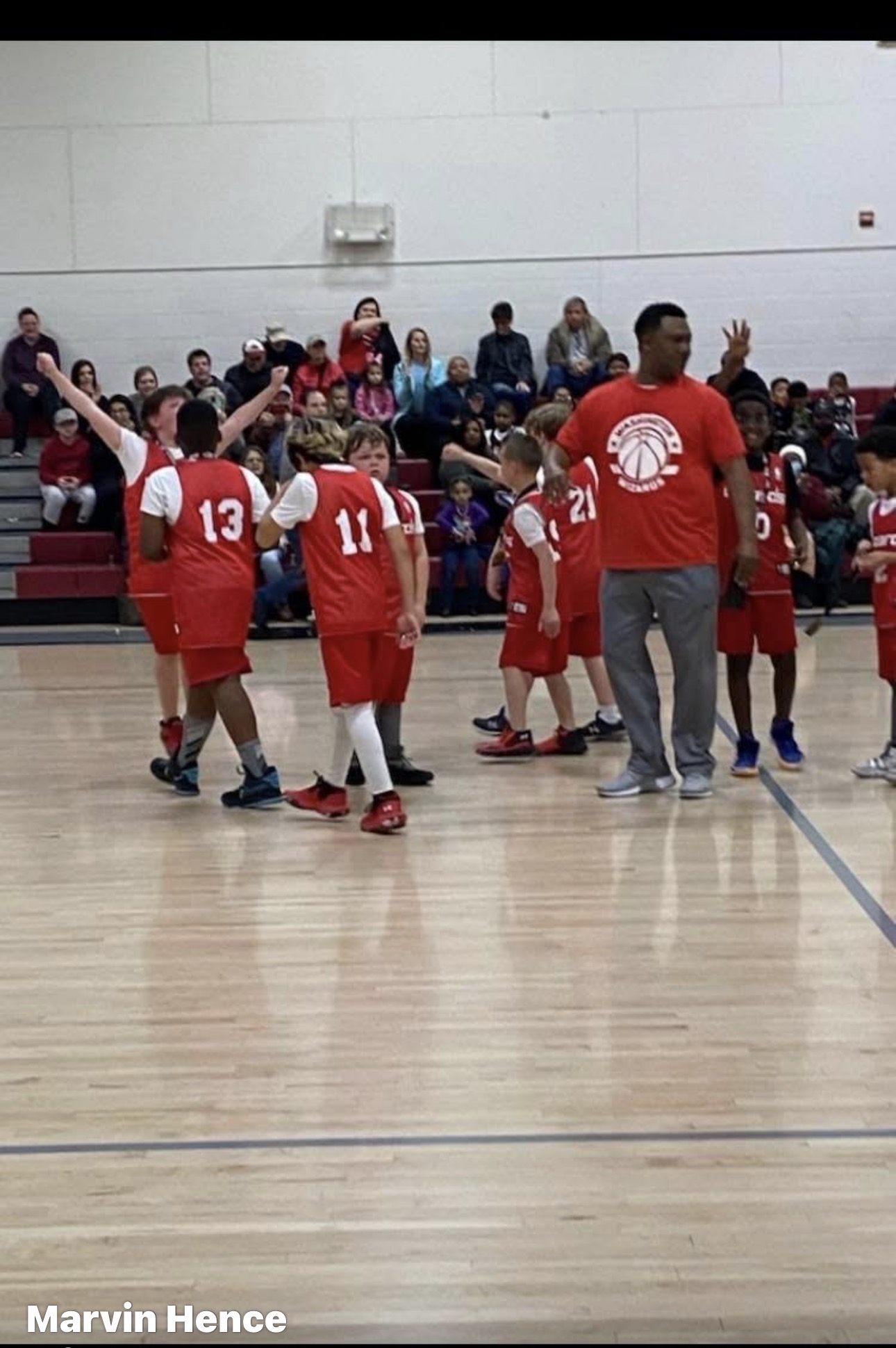 A coach gathering a youth basketball team in a gym huddle