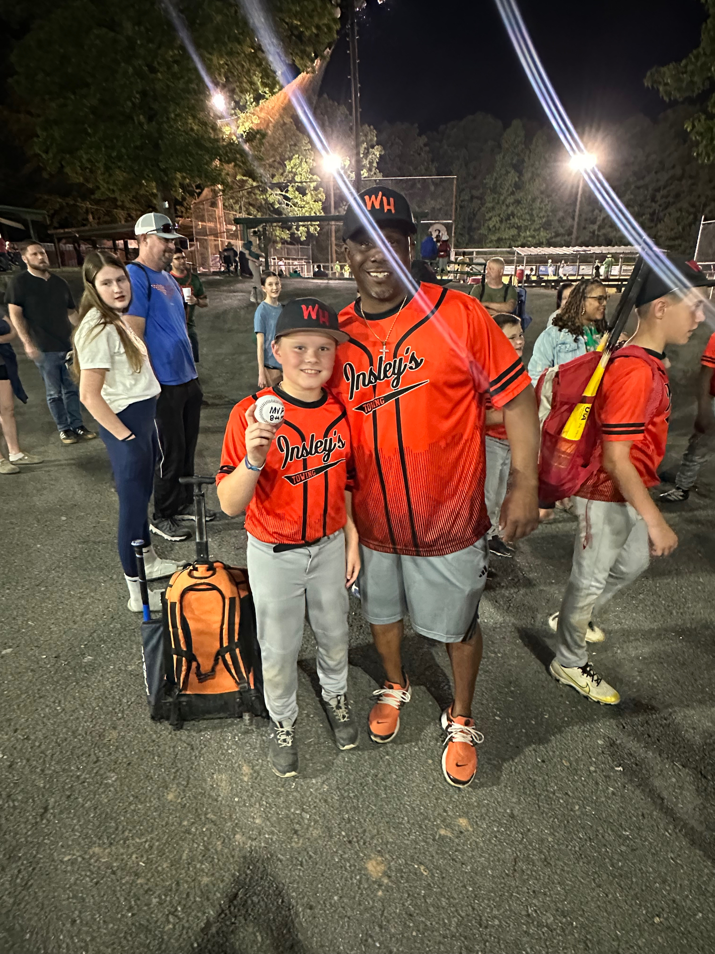 A coach and a young athlete in red jerseys posing with an MVP ball under the field lights at night